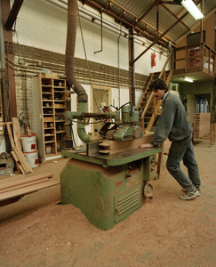 822292 Afbeelding van een werknemer bezig aan een schaafmachine in de werkplaats van Aannemingsbedrijf H.J. Jurriëns ...